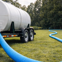 Tanker trailer with a blue hose on grassy area with trees in the background