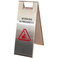 Metal sign with 'Working in Progress' and warning symbol