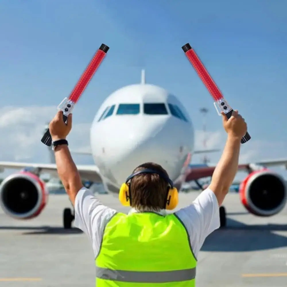 Person in a high-visibility Traffic light Baton holding red and black lights with an airplane 