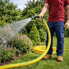 Person watering plants with a yellow garden hose in a garden setting