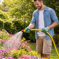 Man watering flowers in a garden with a yellow hose