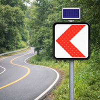 Road sign with a red leftward arrow on a rural road with solar panel