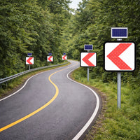 Winding road with multiple left-turn traffic signs and solar panels in a forested area.