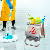 Person cleaning a floor with a mop, wearing a yellow apron and blue gloves, with a 'Caution Wet Floor' sign in the foreground.