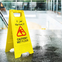 Yellow 'Caution: Wet Floor' sign on a wet floor with Arabic text.